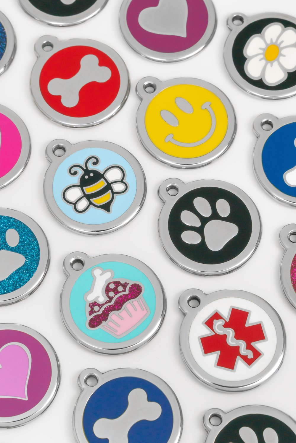 A selection of colourful enamel PetTags Online pet ID tags in paw, bee, heart, bone, daisy and cupcake designs